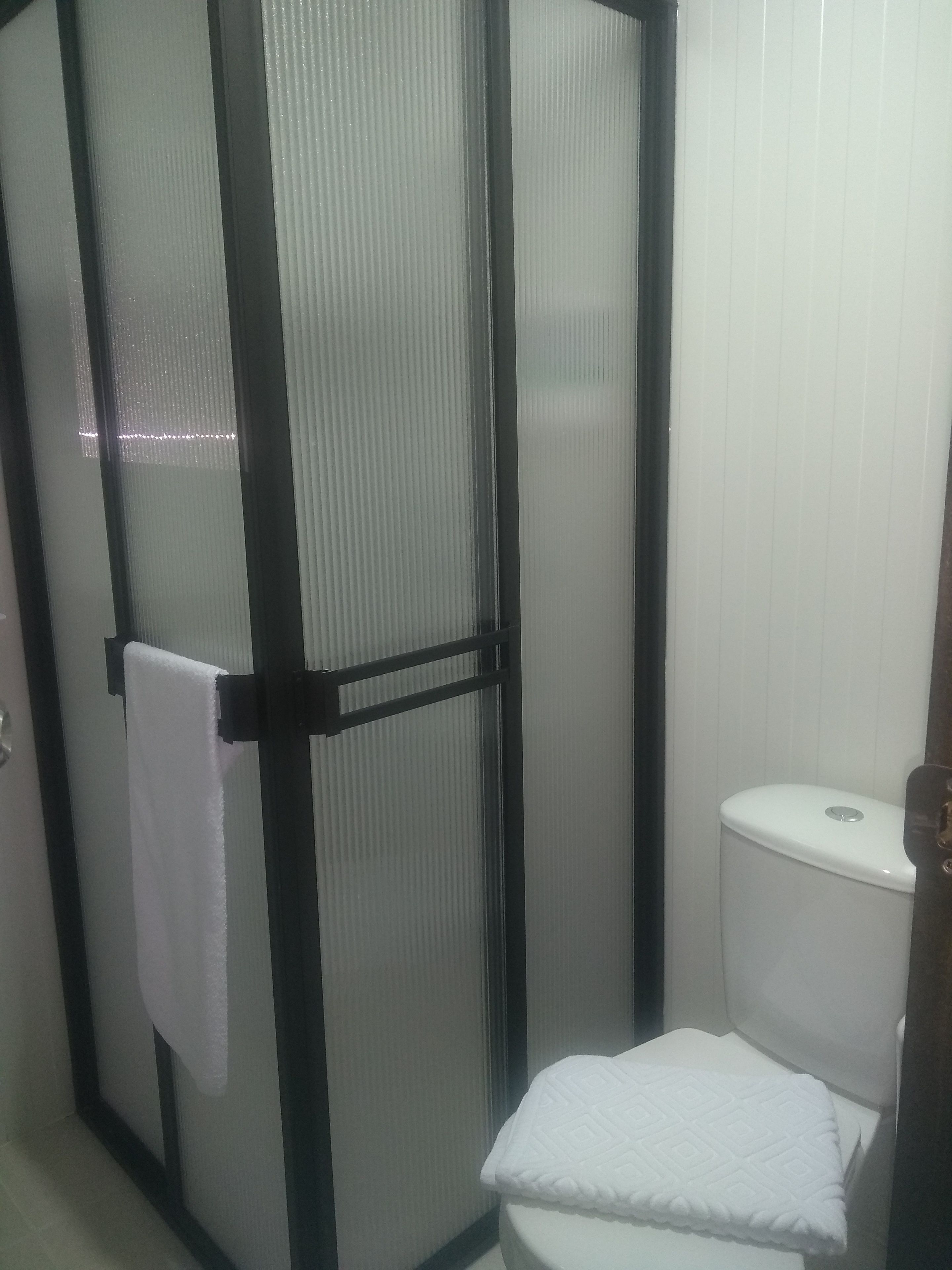 Un baño con inodoro, cabina de ducha y una toalla colgada en la puerta.