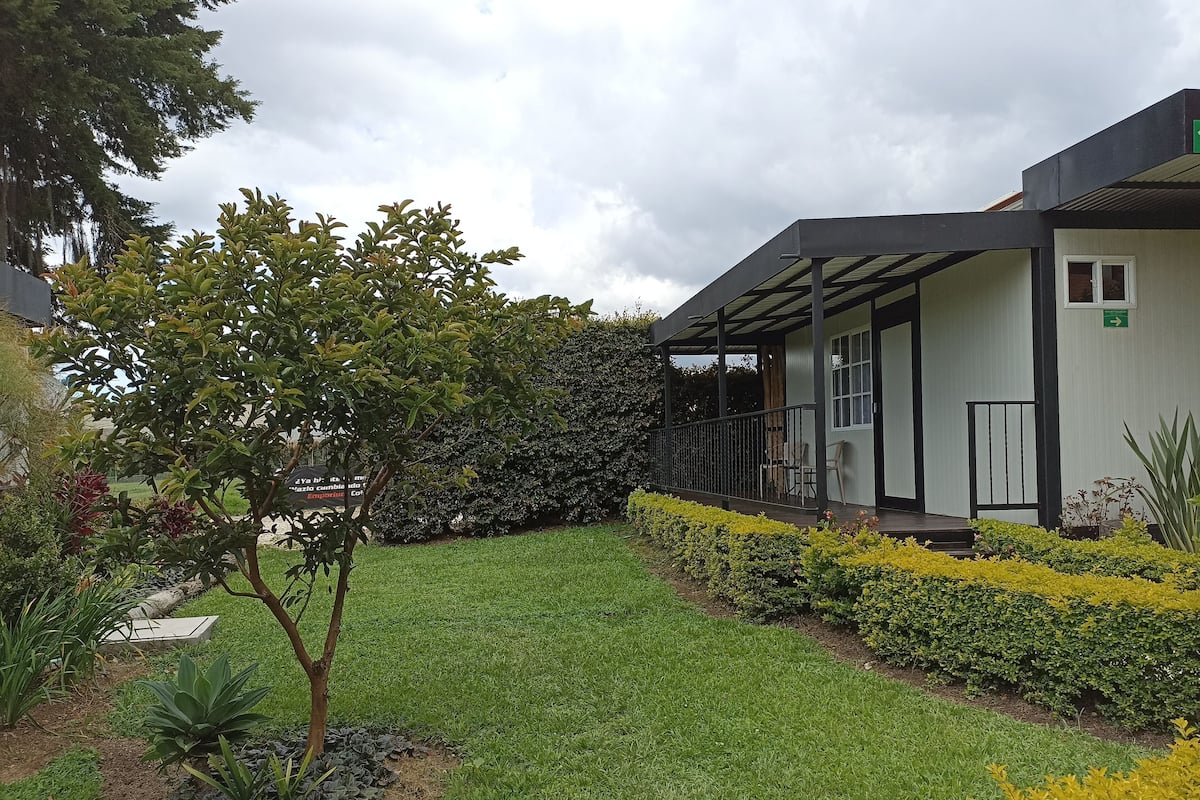 A building with a covered outdoor area, a grassy lawn, and various plants.
