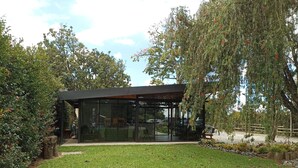Una estructura moderna de vidrio con techo, rodeada de césped cuidado y árboles.
