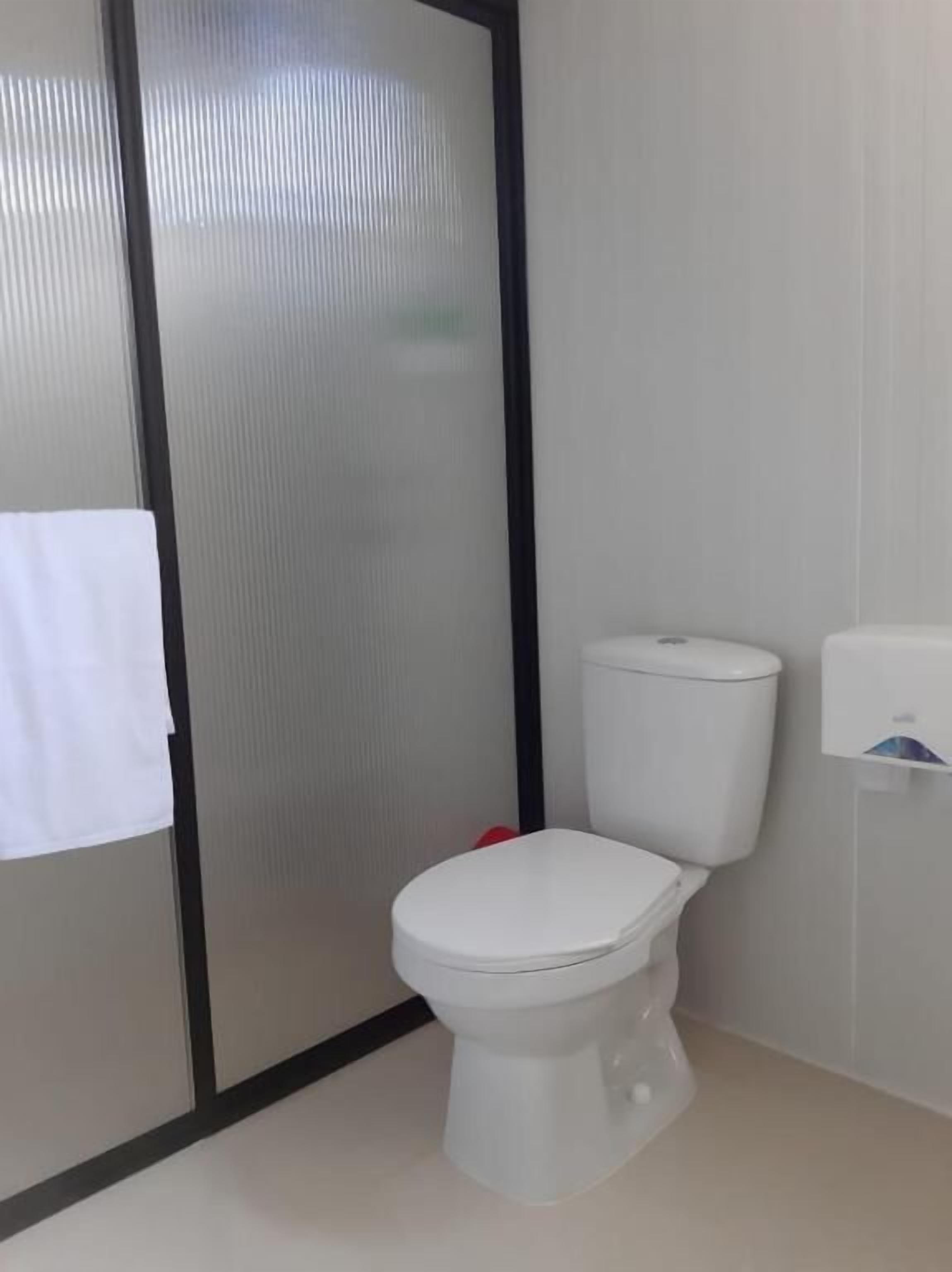 Un baño moderno con inodoro blanco, separador de vidrio y secamanos.