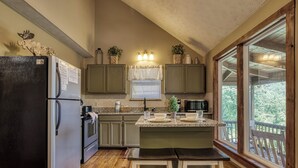 Una cocina con refrigerador, estufa y encimeras de madera. Hay gabinetes, una ventana con persianas y vistas al exterior.
