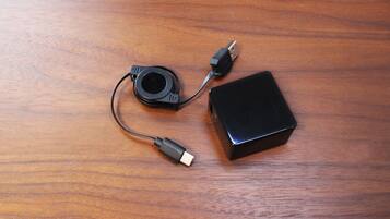 A black electronic device with two cables on a wooden surface.