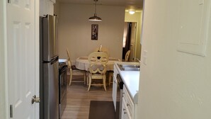 Une cuisine étroite avec un réfrigérateur, une table à manger avec des chaises et un luminaire suspendu.