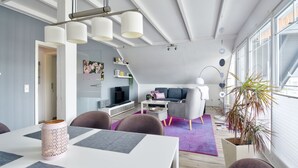 Een moderne woonkamer met een eethoek, grote ramen en een trap.