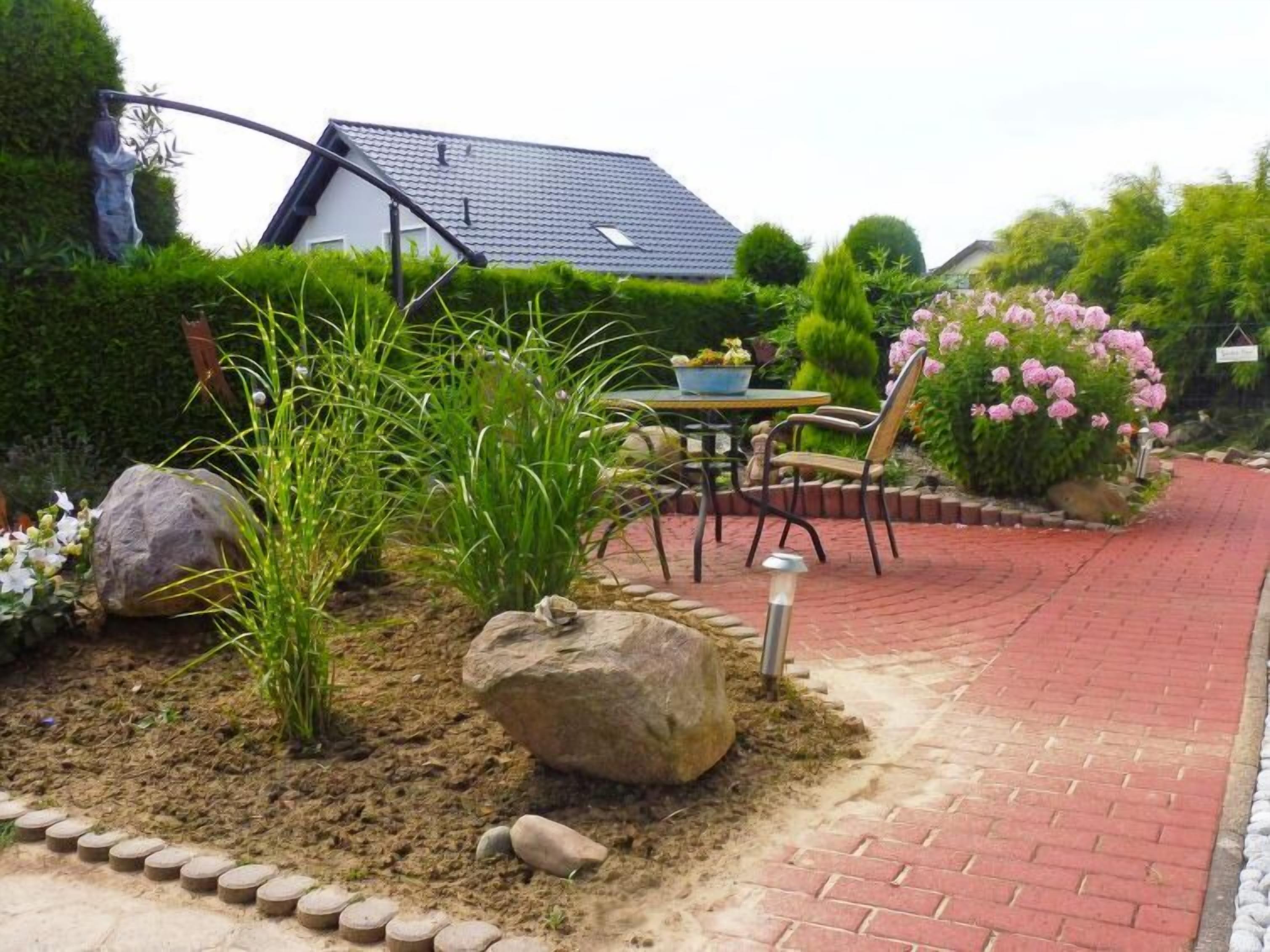 A garden with a paved walkway, a table with chairs, and a house in the background.