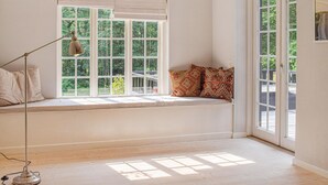 Una habitación con un amplio asiento junto a la ventana, una lámpara de pie y vistas al verdor exterior.