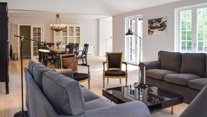 Un salón amplio con un sofá gris, un sillón a juego y un comedor con candelabro.