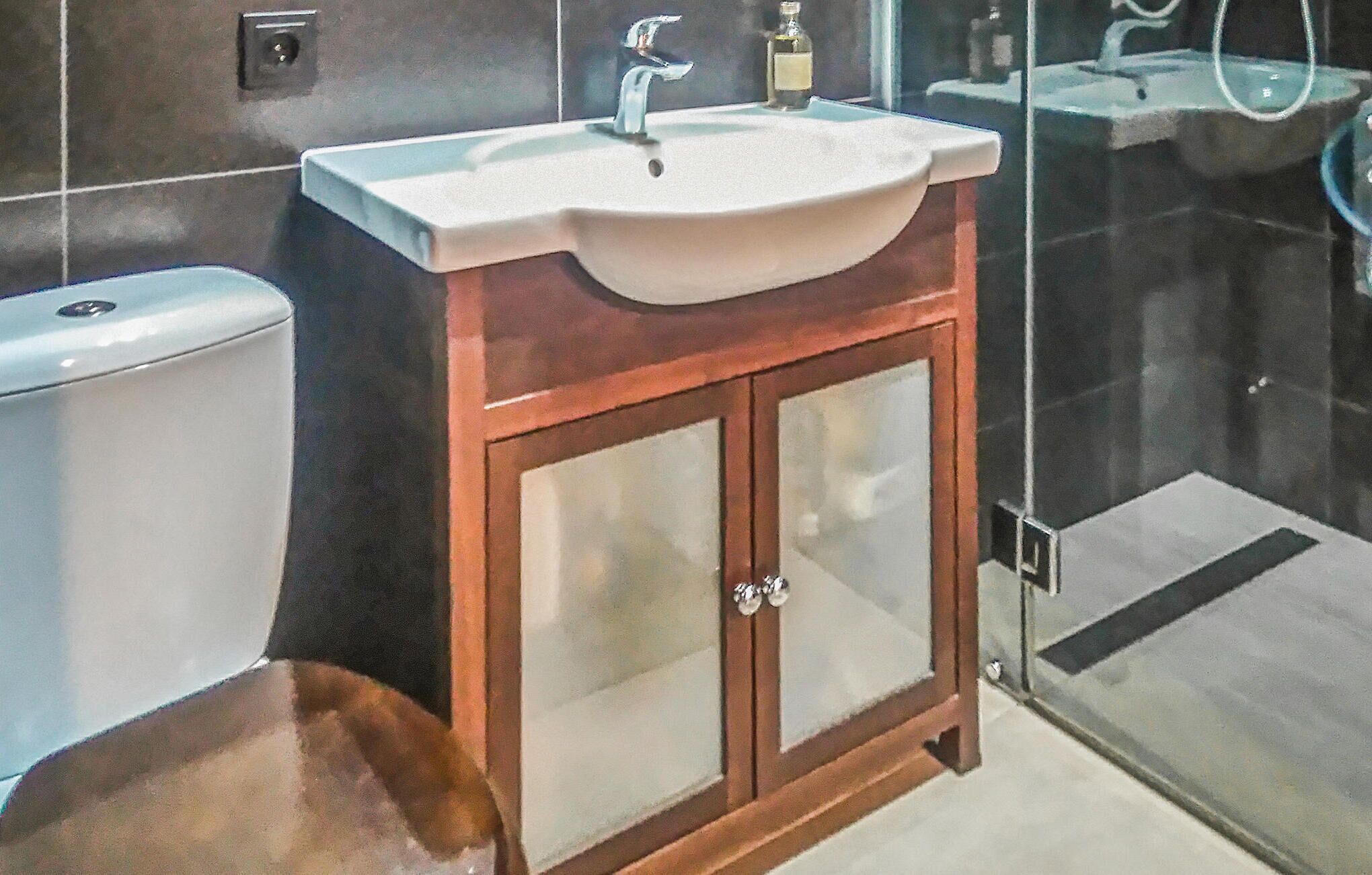 A bathroom with a white sink, wooden cabinet, and a glass shower enclosure.