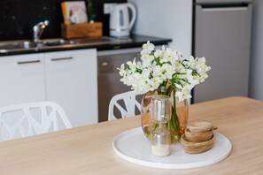 A kitchen with white cabinets, a wooden table, a vase with white flowers, and a small glass container.