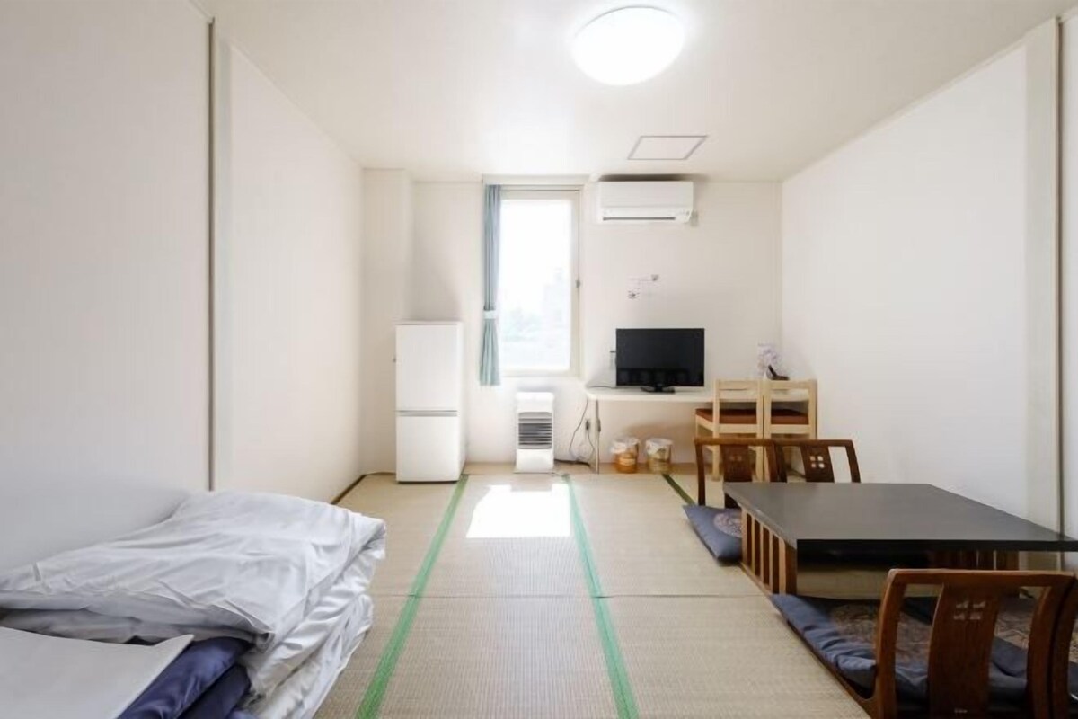 A compact hotel room with a bed, a small desk with a chair, a television, and a window with curtains.