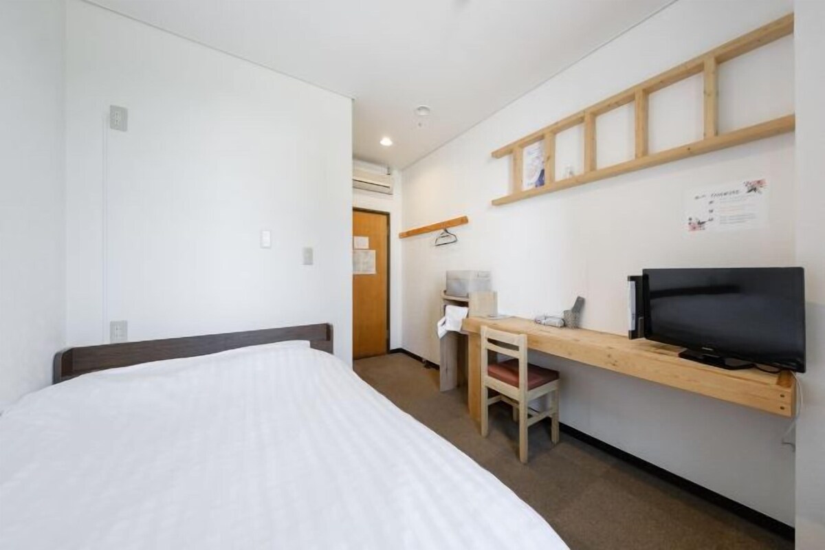 A hotel room with a bed, a desk with a chair, a television, and a wooden shelf.