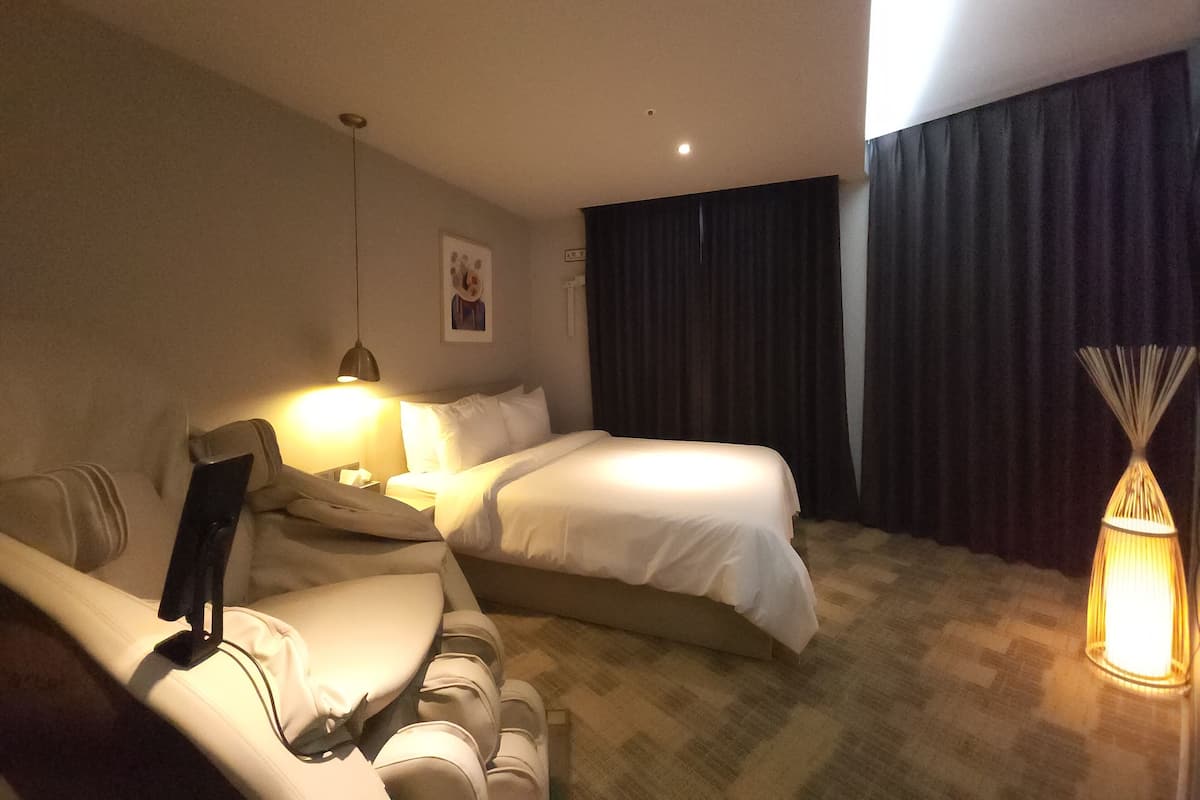 Ein Hotelzimmer mit Bett, Sofa, Lampe und Vorhang.