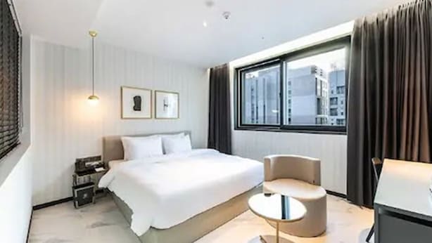 A modern hotel room with a large bed, a round seating area, a desk, and a window with a city view. - Brown Dot Hotel Jinju Chungmugong (Jinju)