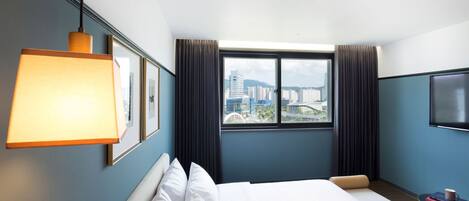 Una habitación de hotel con una cama grande, una ventana con cortinas, un televisor montado y una lámpara colgante.