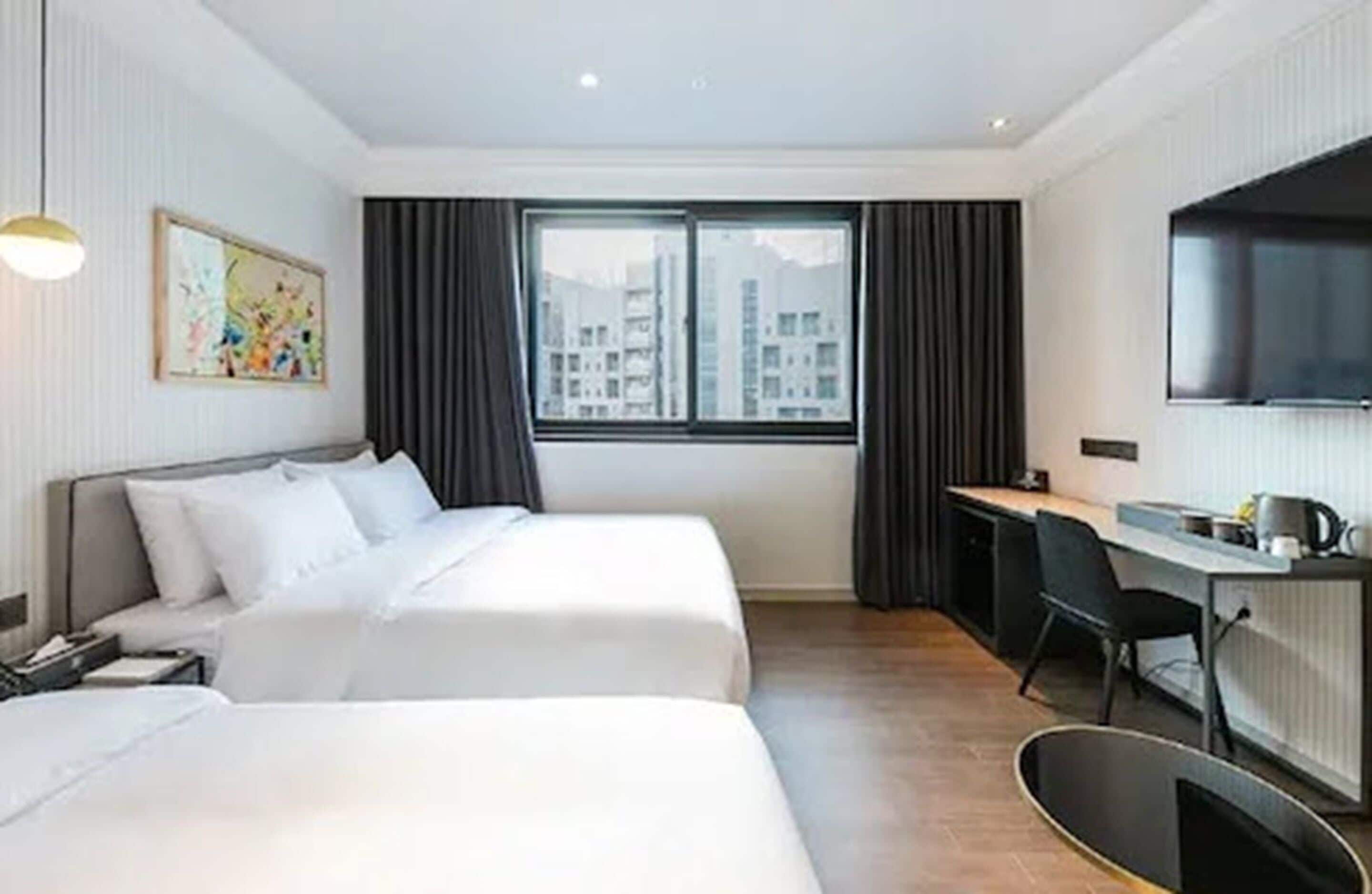 Habitación de hotel con dos camas, un escritorio, una silla, un televisor y una ventana con cortinas.