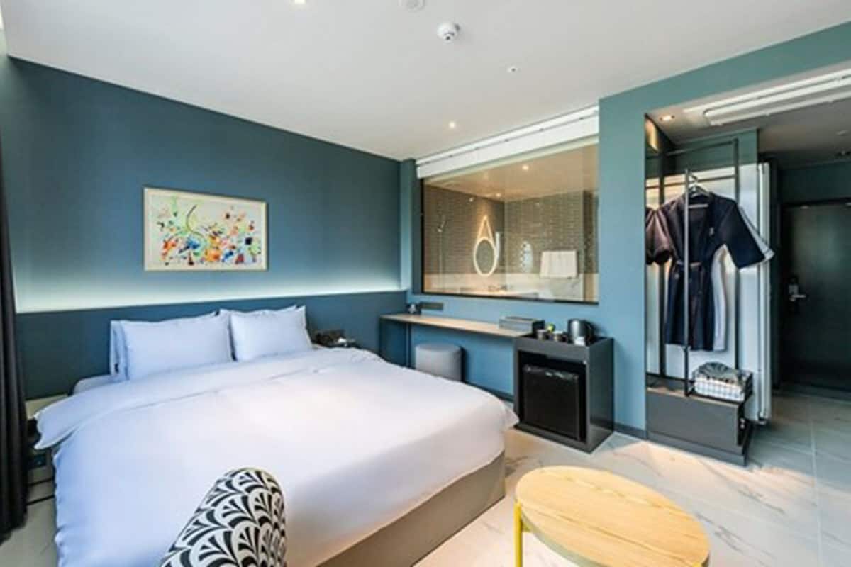 Ein modernes Hotelzimmer mit einem großen Bett, einem kleinen Schreibtisch, einem Spiegel und einer Duschkabine.