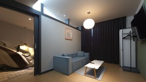 A modern living room with a sofa, a small table, a ceiling light, and a TV mounted on the wall. - Brown Dot Hotel Jinju Chungmugong (Jinju)