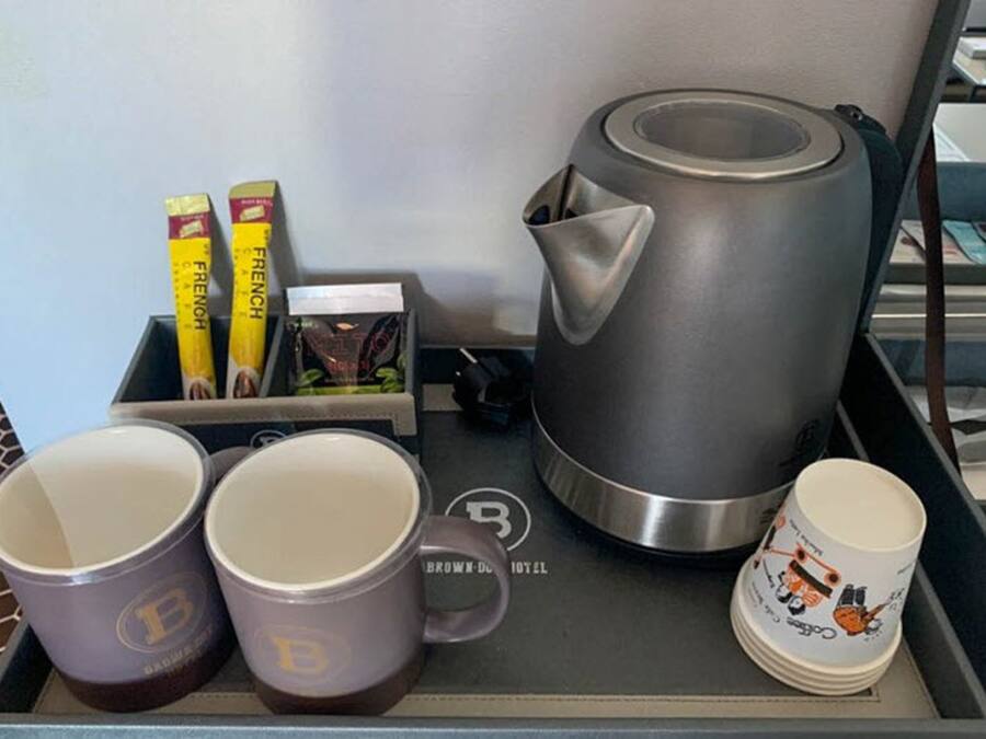 A tray with a French coffee creamer, a box of coffee creamer, a French press coffee maker, and two mugs with a logo.
