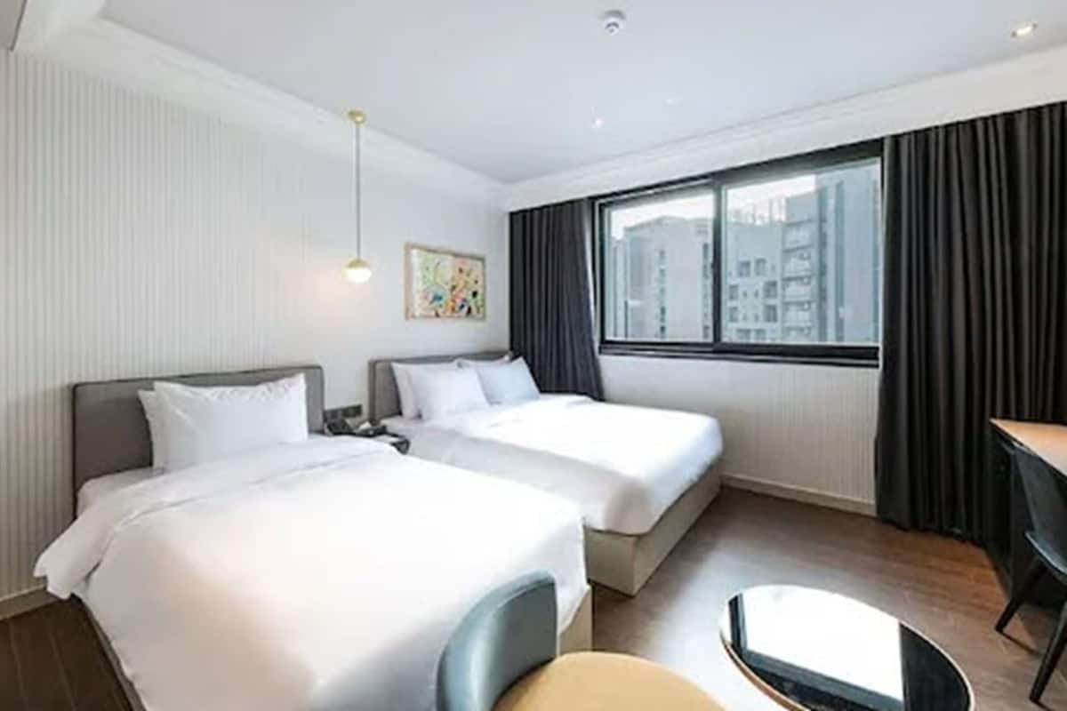 Ein Hotelzimmer mit zwei Betten, einem Schreibtisch und einem fenster mit Vorhängen.