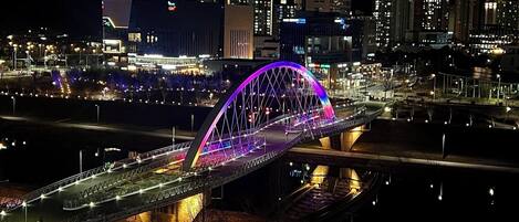 Un puente muy iluminado con un arco de colores de arcoíris, rodeado de edificios y calles de la ciudad por la noche.