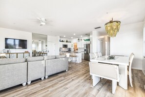 Une cuisine moderne avec des meubles blancs, un coin repas avec une table et des chaises blanches, et un canapé gris.