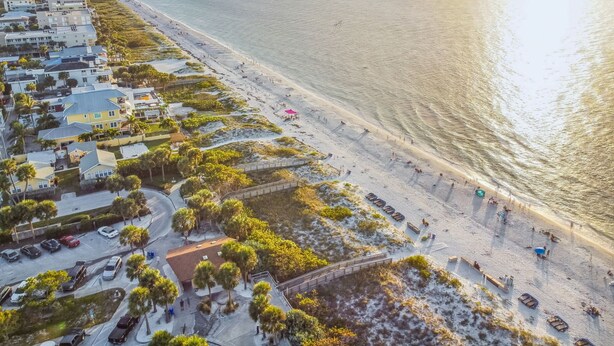 Luchtbeeld van een kustgebied met strand, gebouwen en een parkeerplaats.