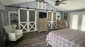 Ein Schlafzimmer mit einem großen Bett, einem Sessel, einem Schminktisch und einem Fernseher.