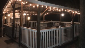 Eine überdachte Terrasse im Freien mit Lichterketten, Holzgeländern und Sitzbereichen.