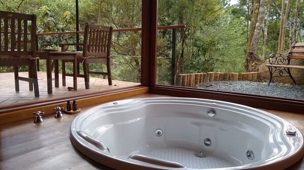 A spa area with a large bathtub, wooden chairs, and a view of a forest. - Pousada Tijupá (Itatiaia)