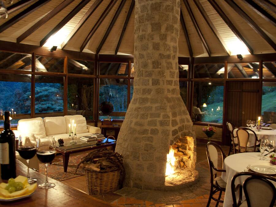 Un interior acogedor con chimenea de piedra, vigas de madera y un comedor con mesas dispuestas para una comida.