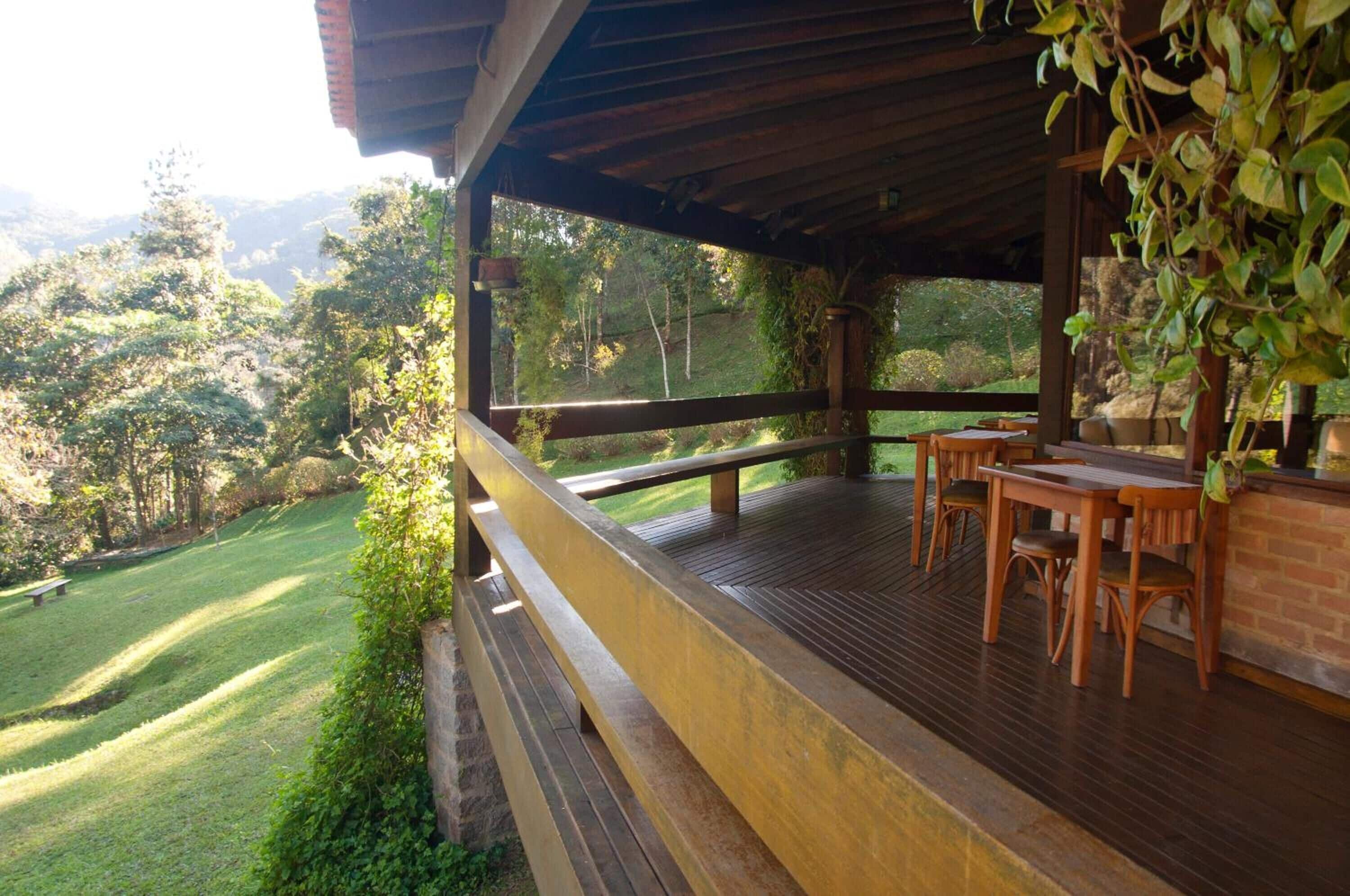 Um deck de madeira com área de estar ao ar livre, cercado por vegetação exuberante e vista para uma paisagem montanhosa.