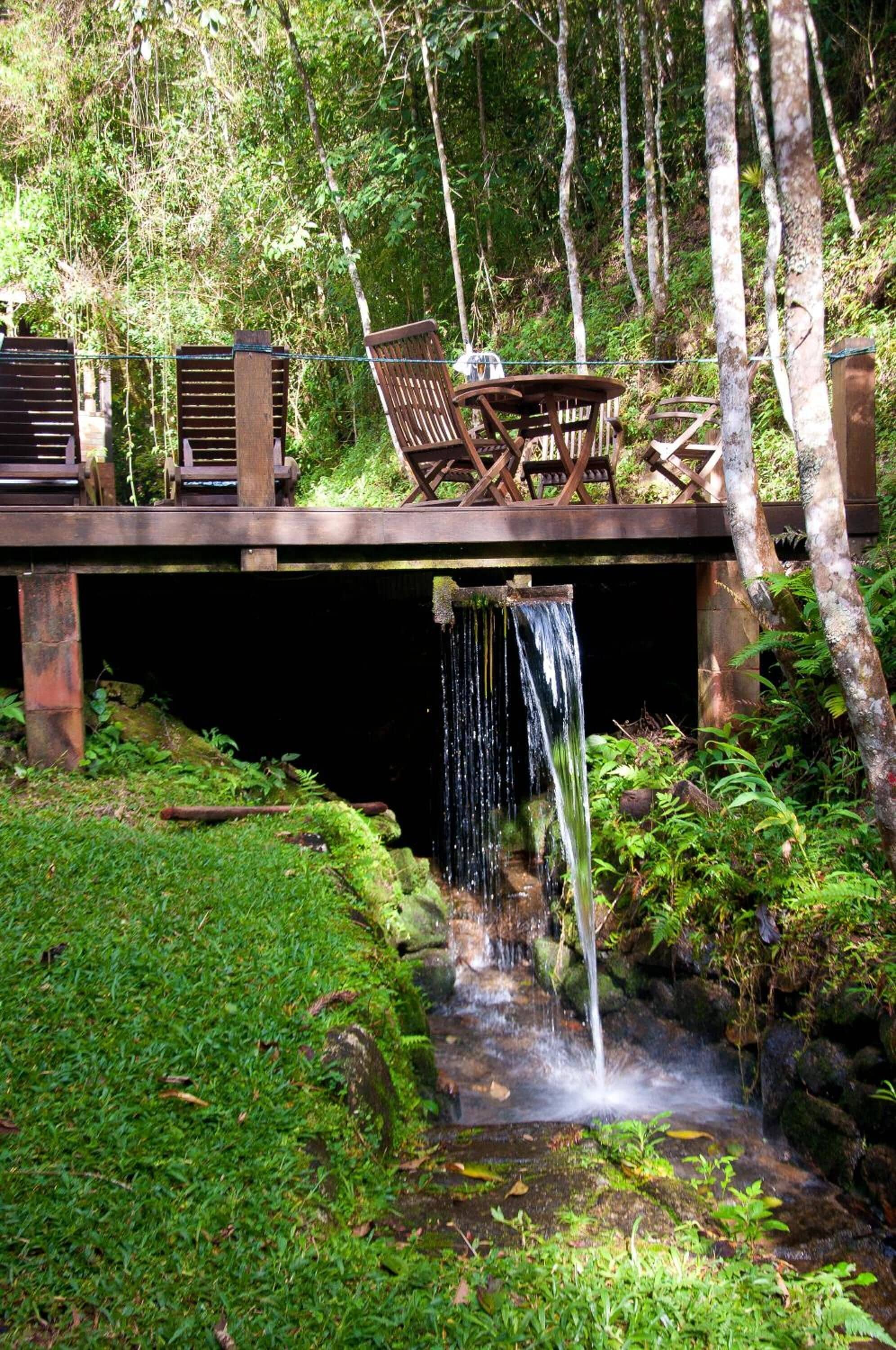 A wooden deck with chairs and a table overlooking a waterfall.