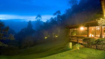 A modern building with a glass facade, surrounded by a lush garden and a hilly landscape.