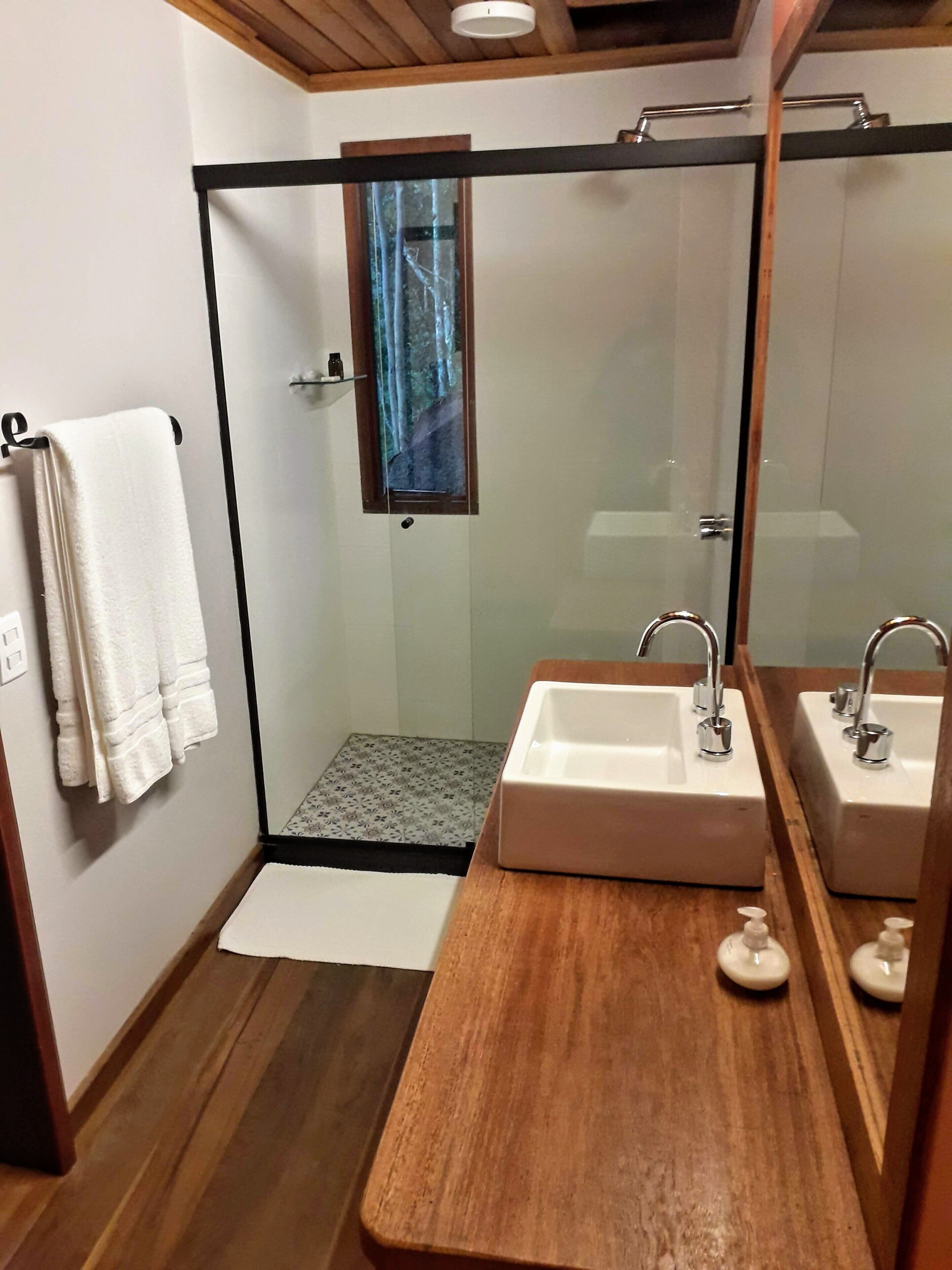 A modern bathroom with a glass shower enclosure, wooden vanity, and a large mirror.