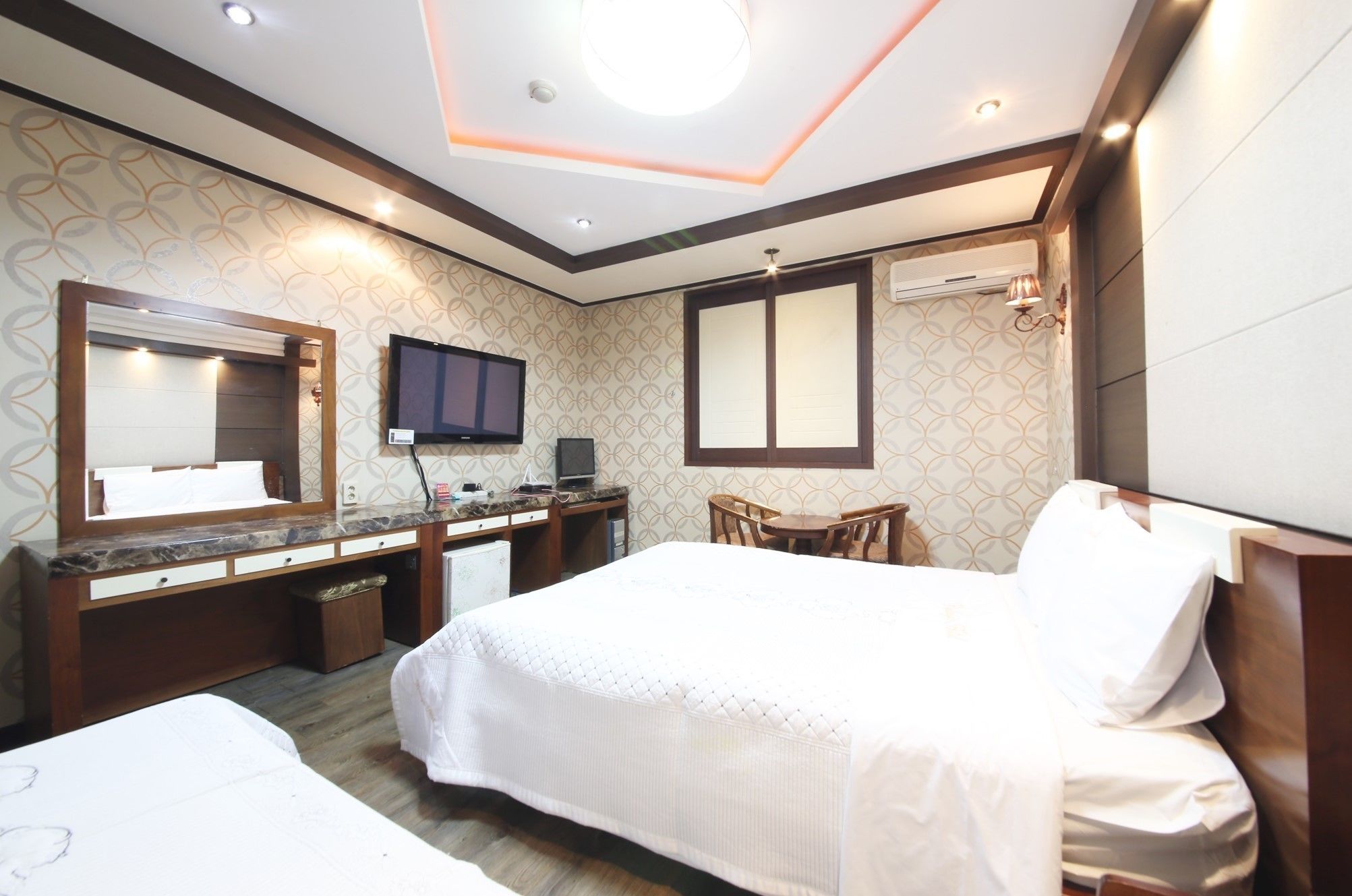 A hotel room with a bed, a desk with a computer, a TV, and a seating area.