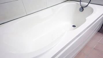 Eine weiße Badewanne mit Ablass, Duschschlauch und gefliestem Boden.