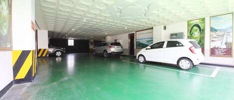 Un estacionamiento con piso verde y techo con diseños circulares. Se ven tres coches aparcados, y un coche blanco está estacionado a la derecha.