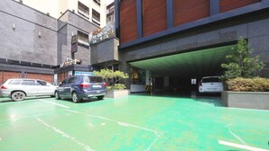 Un espace de stationnement doté d’une surface verdoyante, d’une entrée abritée et d’un bâtiment au design moderne, agrémenté d’un balcon.