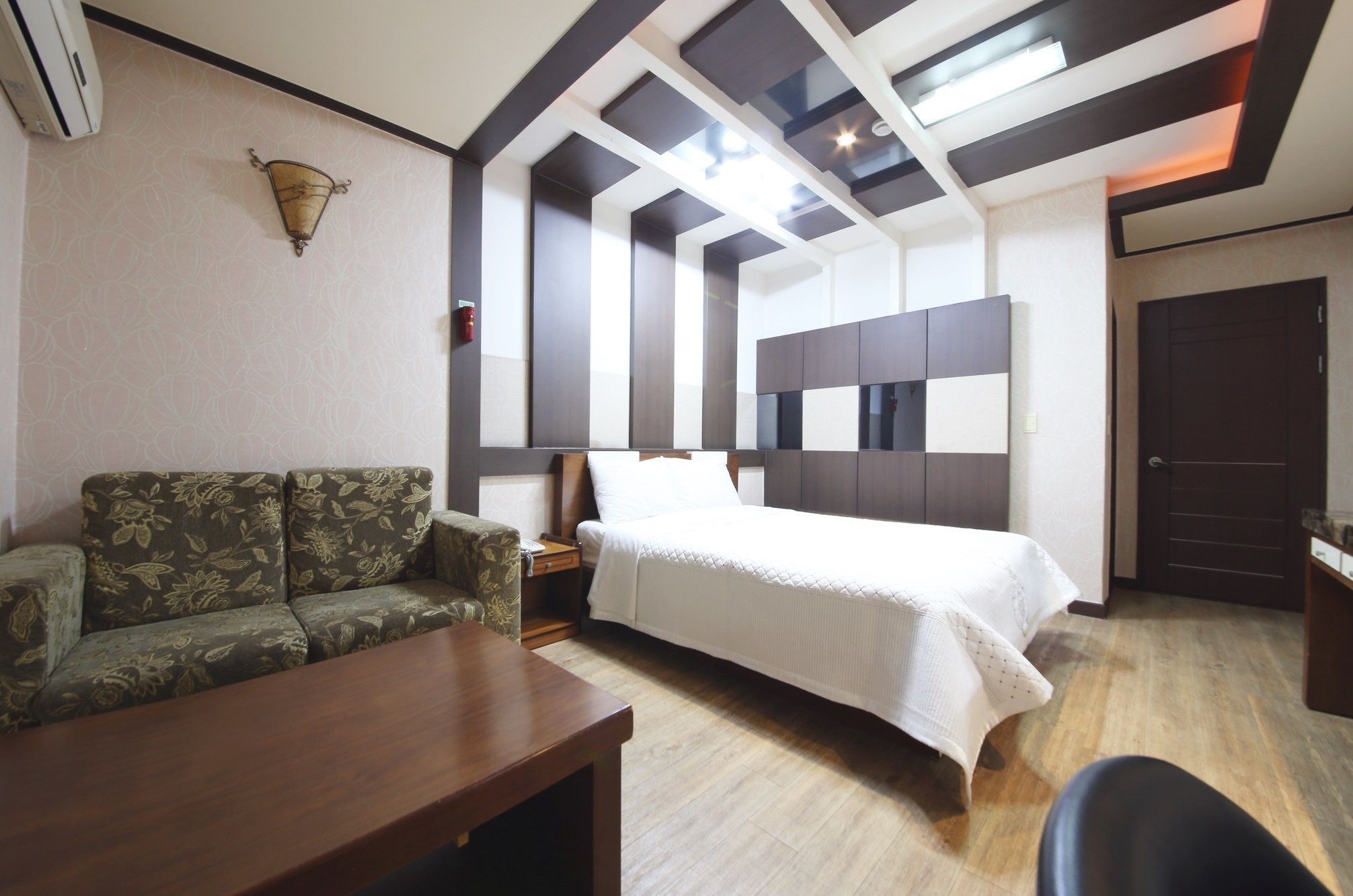 A hotel room with a bed, a sofa, a wooden table, and a desk.