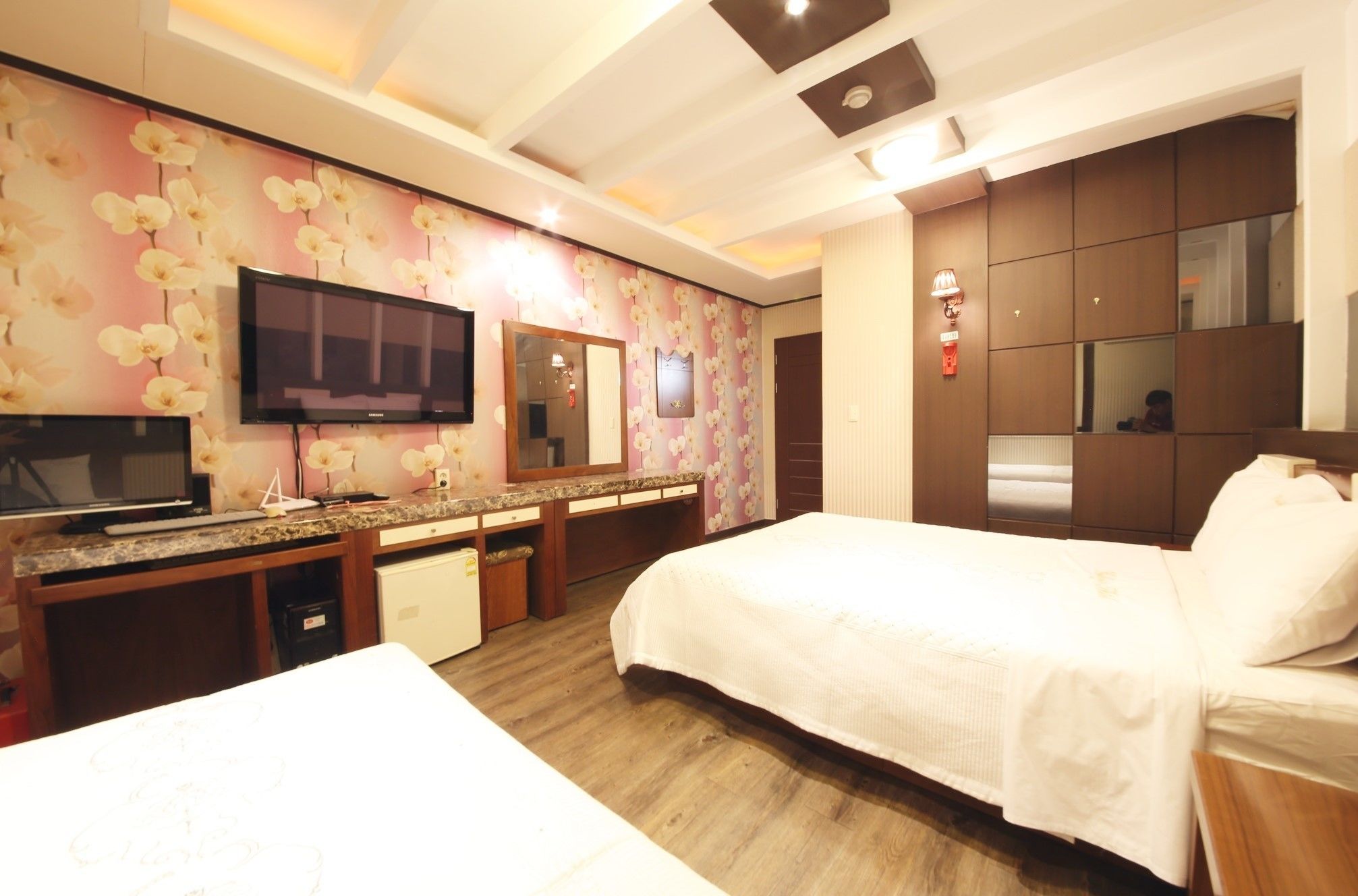 A hotel room with a bed, a TV, a desk with a computer, a mirror, and a wardrobe.