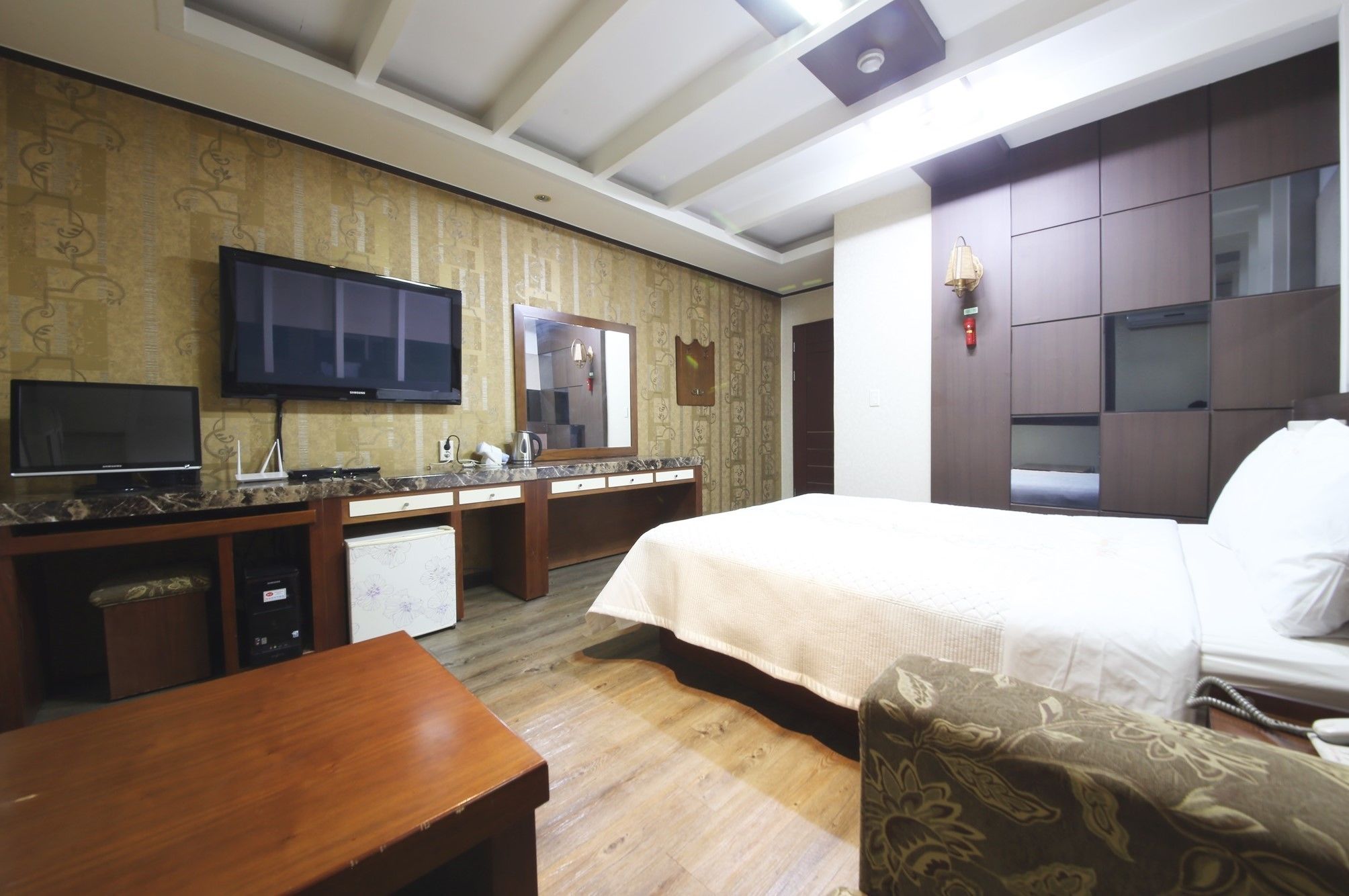 A hotel room with a bed, a desk, a television, a mirror, and a wardrobe.