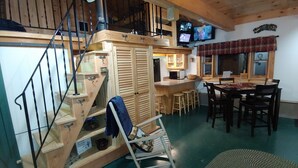 A wooden interior with a staircase, kitchen area, dining table, and two televisions.