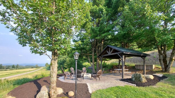 A covered outdoor seating area with a table and chairs, surrounded by a landscaped garden with rocks and a tree.