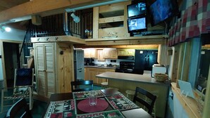 A cozy cabin interior with a dining area, kitchen, and upper sleeping quarters.