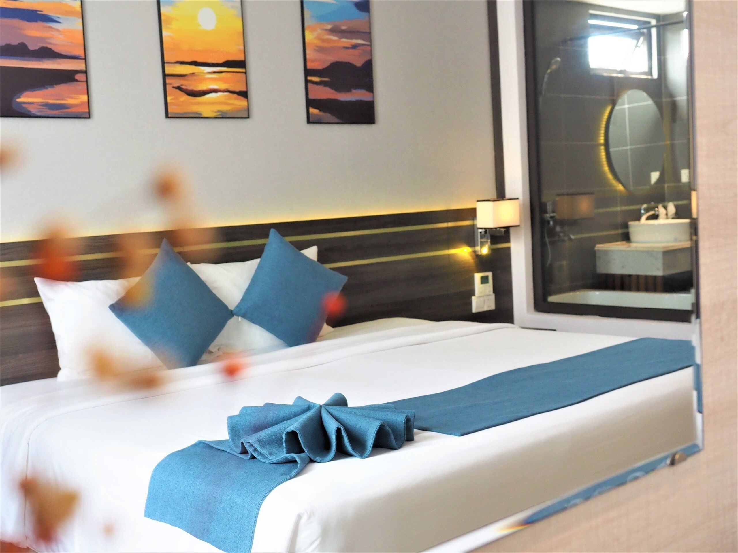 Habitación de hotel con cama, almohadas, mesita de noche, lámpara y espejo de baño.