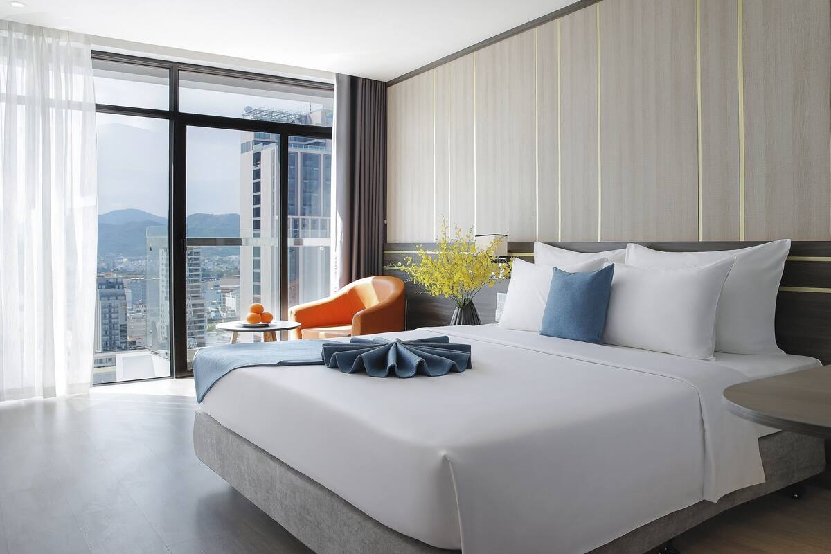 A modern hotel room with a large bed, a view of the city, and a cityscape visible through the window.