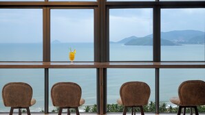 A view from a window with three chairs facing a body of water and distant mountains. - Seana Hotel (Nha Trang)
