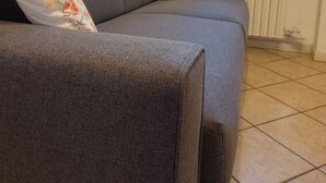 Ein graues Sofa mit blumigen Kissen, eine Heizung und ein Fenster mit Vorhängen.