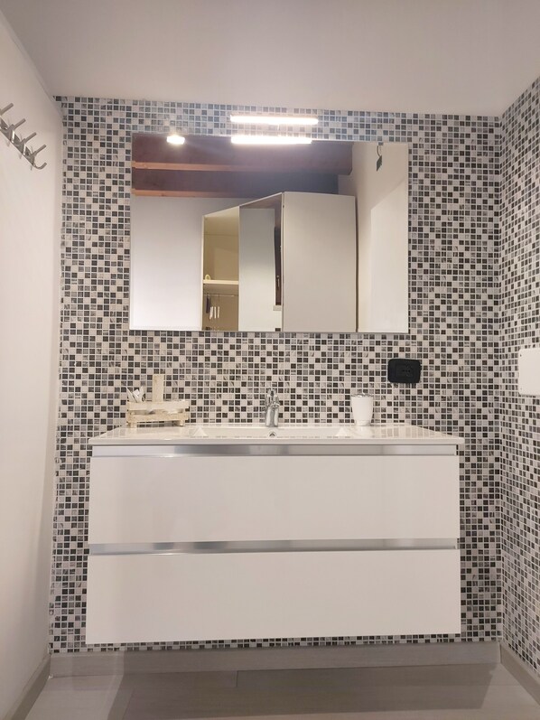 Un baño moderno con tocador blanco, un espejo grande y salpicadero de azulejos.