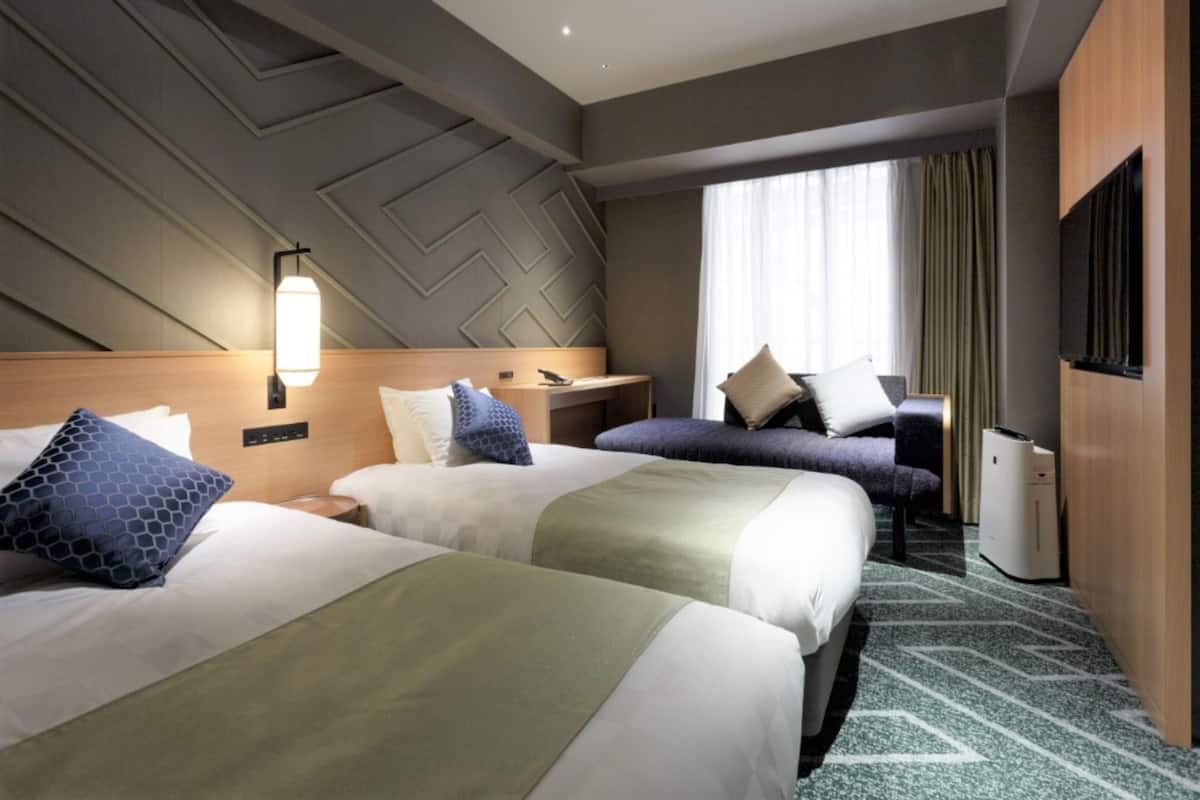 Habitación de hotel con dos camas, un escritorio, un televisor y una ventana con cortinas.